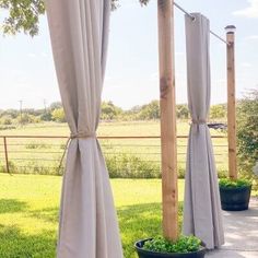 an outdoor area with curtains and potted plants on the ground near a wooden fence