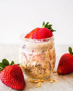 two strawberries sit next to a jar of oatmeal