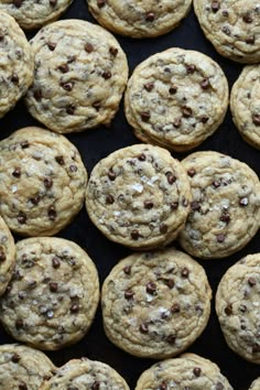 chocolate chip cookies sitting on top of a black table next to a pile of other cookies