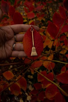 a person holding a red leaf with a gold keychain hanging from it's end