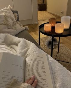 someone is reading a book in their living room with candles on the side table and coffee table