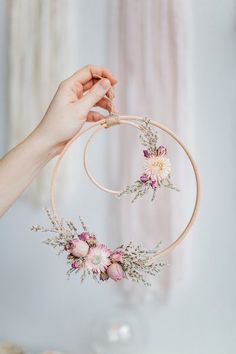 a hand holding a hoop with flowers hanging from it's side and another hand holding the hoop