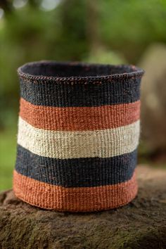 an orange, black and white striped basket sitting on top of a tree stump in the woods