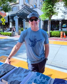 a man standing in front of a table full of shirts and books on the street