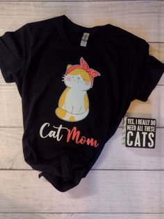 This crazy cool "Cat Mom" graphic is a full color DTF design, pressed onto a T Shirt.  The Gildan G500L Women's t-shirt is the perfect choice for a basic t-shirt designed for her. The 100% jersey knit cotton absorbs moisture, making this a great choice to wear as an undershirt or by itself on warm days. The long, loose length of the shirt provides you with carefree bending, flexing, and moving. *Care instructions:- Turn inside out and machine wash on cool or warm setting. It is preferable to hang dry for longest life, but can be machine dried on low setting. Do NOT iron the design. It will melt. Use a pressing cloth. **Please see the size chart** We do not accept returns or exchanges Funny Black Top With Cat Design, Funny Black Cat Design Top, Trendy Black T-shirt For Gift, Funny Black T-shirt With Cat Design, Cute Black T-shirt With Cat Design, Trendy Black T-shirt With Cat Print, Fun Black T-shirt As A Gift, Novelty Black T-shirt As A Gift, Novelty Black T-shirt For Gift