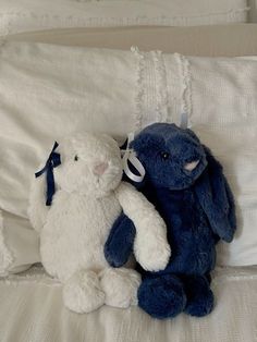 two stuffed animals sitting on top of a bed next to each other, one blue and the other white