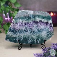 a blue and purple stone sitting on top of a metal stand next to flowers with candles in the background