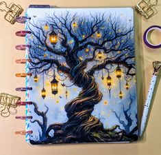 a spiral notebook with a tree and lanterns on it next to a pair of scissors