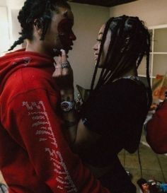 two people with dreadlocks standing next to each other and one is holding something in his mouth