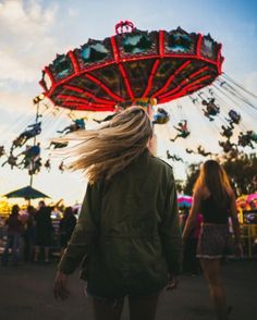 a woman standing in front of a carnival ride with her hair blowing in the wind