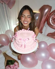 a woman sitting in front of a cake with pink frosting and balloons around her