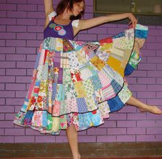 a woman is dancing in front of a purple brick wall wearing a multicolored skirt