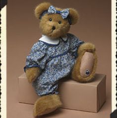 a brown teddy bear sitting on top of a box wearing a blue dress and hat