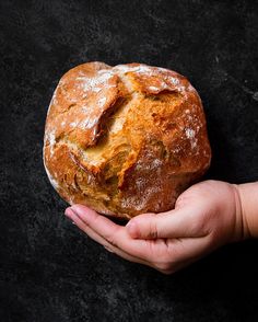 a person holding a loaf of bread in their hand on a black surface with some powdered sugar