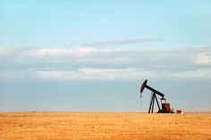 an oil pump sitting in the middle of a dry grass field next to a blue sky