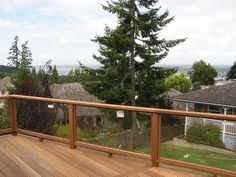 a wooden deck with railings and trees in the back ground, looking out at houses