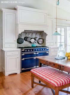 a kitchen with white cabinets and blue stove top oven in the center, along with a red bench