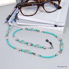 Make a bold fashion statement with this teal blue green beaded eyeglass chain! Classy and sophisticated, great for wearing around the office. Our beaded chains make for a great gift? Rubber loops adjust to fit most glasses frames.   🦉Product Details:  * Approx. Length - 30 in (including rubber loops) * Chain Weight: 1.6 oz * Bead Color(s): Teal Blue Green * Metal Color: Silver-tone * Material: Glass and Czech Beads * Closure: Lobster Claw Clasps and Rubber Loop Ends * Product ID: G238 🎁 Gift packaging available at Checkout ($4.00 USD) - See last image   🦉NOTES: * Not recommended for young children! * The lobster clasps make replacement of the rubber loops easy if they break. * All measurements and weights are approximate and may vary slightly from the listed dimensions. * Some photos ma Blue Beaded Chain Glasses Chains With Round Beads, Blue Beaded Glasses Chains, Blue Glasses Chains With Round Beaded Chain, Blue Beaded Glass Glasses Chains, Trendy Blue Glass Glasses Chains, Elegant Adjustable Blue Glasses Chains, Elegant Blue Adjustable Glasses Chains, Trendy Blue Glasses Chains As Fashion Accessory, Elegant Turquoise Glass Beaded Necklace