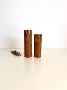 two wooden vases sitting next to each other on a white counter top with a dried plant in between them