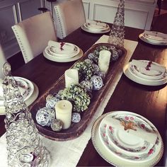 a dining room table set for christmas with plates, candles and decorations on the table