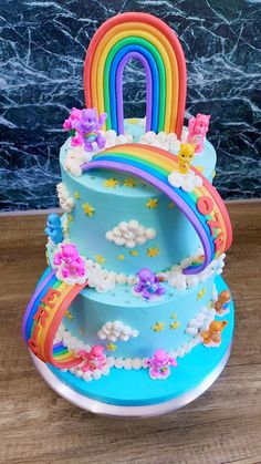 a multi layer cake with rainbows and clouds on the top, sitting on a wooden table