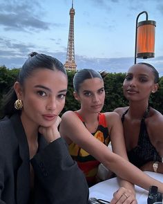 three beautiful women sitting at a table with the eiffel tower in the background