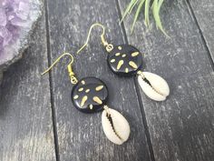 These gorgeous dangle earrings feature genuine off-white sliced moneta cowrie shells dangling beneath 20mm round carved black and gold acrylic beads an etched Afrocentric abstract pattern. Aching for acrylics? Check out the rest of my acrylic jewelry here: https://etsy.me/2IadiWZThroughout Africa and the Americas, cowrie shells have historically been viewed as symbols of womanhood, fertility, and prosperity. Check out my other cowrie shell jewelry here: https://etsy.me/2VQS0r0These earrings meas Black Round Summer Jewelry, Handmade Black Earrings For Beach, Black Drop Earrings For Summer, Black Dangle Jewelry For Beach, Black Shell Jewelry For Gifts, Black Shell Jewelry Gift, Black Shell Jewelry As A Gift, Handmade Black Jewelry For Vacation, Handmade Black Jewelry For Beach