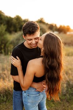 a young man and woman are kissing in the middle of an open field at sunset