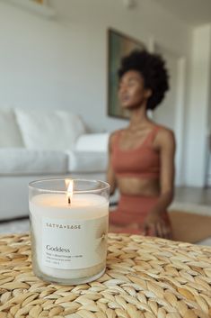 a woman sitting in front of a white couch next to a candle on top of a table