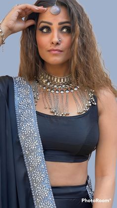 a woman in a black outfit with silver jewelry on her head and hands behind her head