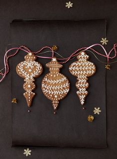 three ornaments hanging from a string on top of a black piece of paper with snowflakes around them