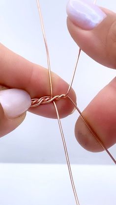 two hands are holding some wire and one hand is using it to make an ornament