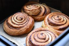 four cinnamon rolls sitting on top of a piece of wax paper in an air fryer