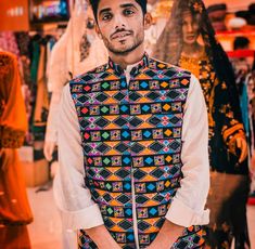 a man standing in front of a store display wearing a colorful vest and white shirt