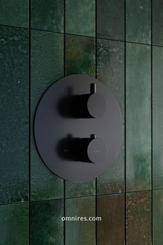 a bathroom wall with green tiles and a black toilet paper dispenser