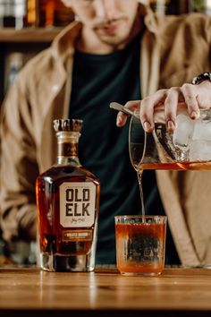 a man pouring an old elk whiskey into a glass on top of a wooden table