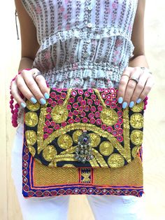 Our new bold embellished clutches come in new statement square shape and are beautiful handmade by local artisans of the Banjara tribe in India. Embellished with bold metallic thread these bags are a stunning accessory to any outfit. All bags are hand-crafted using patchworks of vintage Banjara embroidery and embellishments. According to some authorities, the Banjara lineage goes back some 2000 years. Wear as an over-sized clutch or on your shoulder with the light-weight cotton pompom chain.  Be Tribes In India, Boho Clutch, Embellished Clutch, Embroidered Clutch, Handmade Clutch, Statement Bag, Colorful Bags, Simple Chic, Boho Vintage