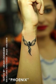 a woman is holding her arm up with a bird tattoo on it's wrist