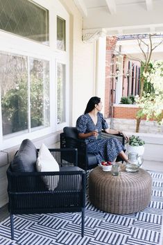 a woman sitting on top of a black chair in front of a white building next to a coffee table