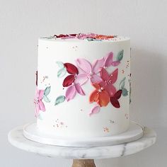 a white cake with pink and red flowers on it sitting on top of a marble stand