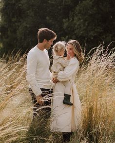 a man and woman standing in tall grass holding a baby