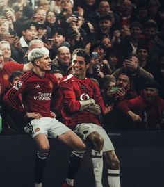 two men in red jerseys are playing soccer while people watch from the stands behind them