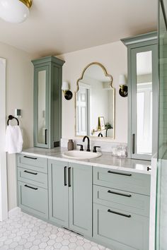 a bathroom with green cabinets and white marble counter tops, along with a large mirror on the wall