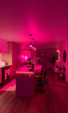 a living room filled with furniture and pink lighting on the walls, along with hardwood flooring