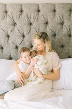 a woman holding a baby while sitting on top of a bed