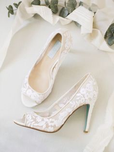 a pair of wedding shoes sitting on top of a white cloth covered floor next to flowers