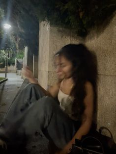 a woman sitting on the ground with her hand up to her face while she is smiling