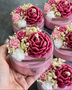 pink and white flowers are in small glass containers on a table with someone's hand