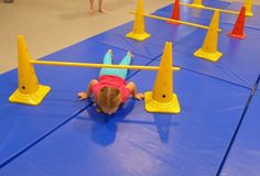 a child is upside down on an obstacle course with cones and poles in the background