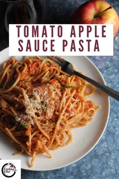 a white plate topped with pasta covered in tomato sauce and parmesan cheese next to an apple